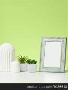 empty white wooden photo frame and flowerpots with plants on white table, green background