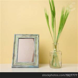 empty white wooden photo frame and green plants on white table, yellow background