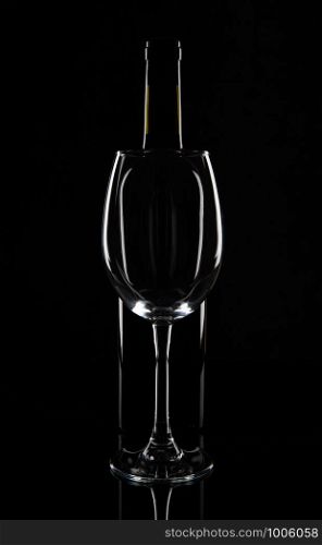 Empty wine glass in front of the wine bottle, isolated on black background.. Empty wine glass in front of the wine bottle, isolated on black background