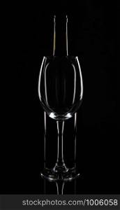 Empty wine glass in front of the wine bottle, isolated on black background.. Empty wine glass in front of the wine bottle, isolated on black background