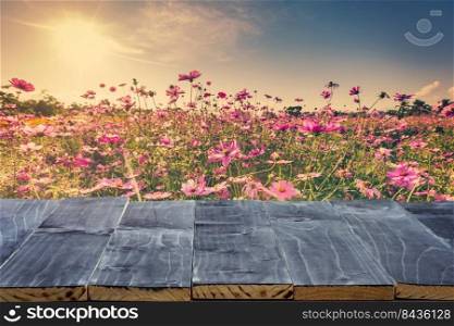 Empty wood table top for product display montage and cosmos flower and sunlight in garden.