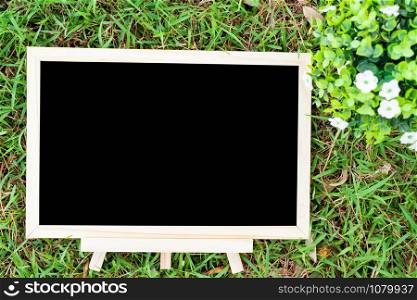 empty wooden blackboard and Flowerpot in square shape on green grass in the park background.