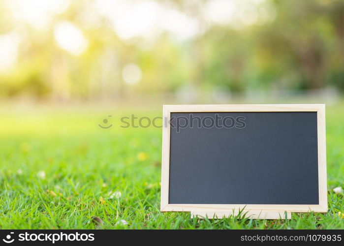 empty wooden blackboard in square shape on green grass in the park background.