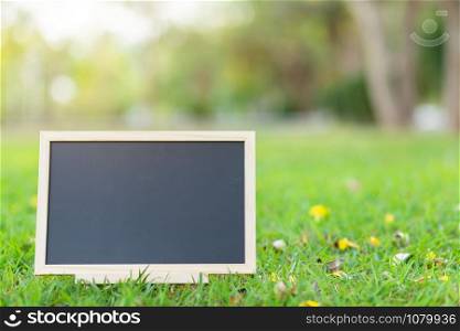 empty wooden blackboard in square shape on green grass in the park background.