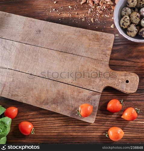 Empty wooden board, tomatoes, bowl with quail eggs and walnut slices on an old wooden table with copy space. Salad Ingredients. Top view. Ripe tomatoes, quail eggs in a bowl and nut crumbs on a wooden board with a toe with an empty board and copy space. Salad preparation concep. Top view