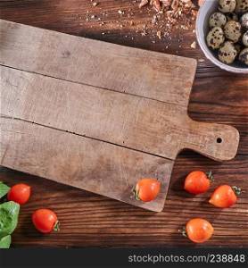 Empty wooden board, tomatoes, bowl with quail eggs and walnut slices on an old wooden table with copy space. Salad Ingredients. Top view. Ripe tomatoes, quail eggs in a bowl and nut crumbs on a wooden board with a toe with an empty board and copy space. Salad preparation concep. Top view