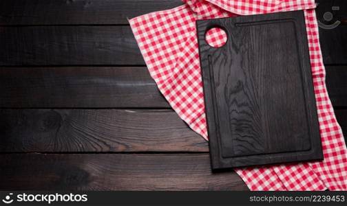 empty wooden cutting board and folded red and white cotton kitchen napkin on a wooden brown background, top view, copy space