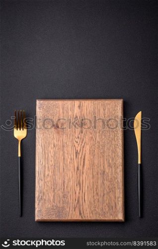 Empty wooden cutting board on dark textured concrete background. Cutlery, preparation for dinner