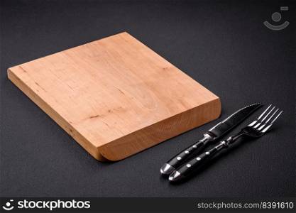 Empty wooden cutting board on dark textured concrete background. Cutlery, preparation for dinner