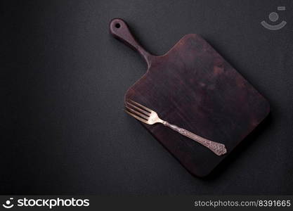 Empty wooden cutting board on dark textured concrete background. Cutlery, preparation for dinner