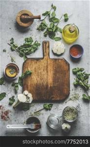 Empty wooden cutting board on grey concrete kitchen table with herbs ,spices, garlic,oil and mortar and pestle. Preparing homemade marinade for meat or vegetables at home.Top view . Frame.