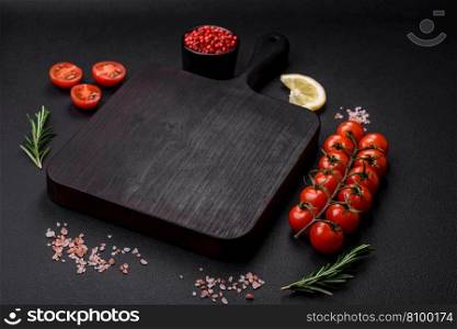 Empty wooden cutting board with cherry tomatoes, spices, salt and herbs on dark concrete background