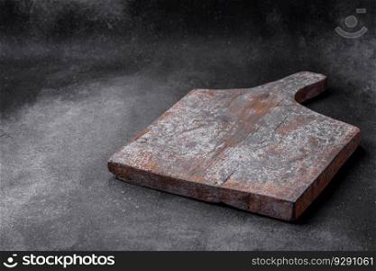 Empty wooden cutting board with cracks and scuffs located on a dark concrete background