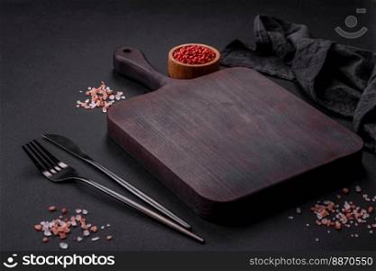 Empty wooden cutting board with spices and herbs on dark concrete background