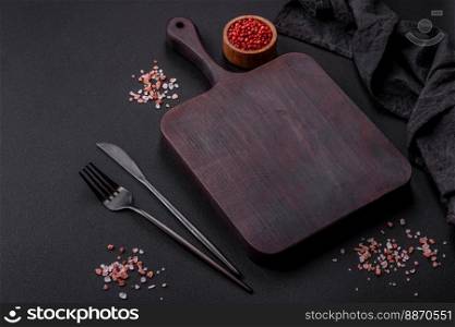 Empty wooden cutting board with spices and herbs on dark concrete background