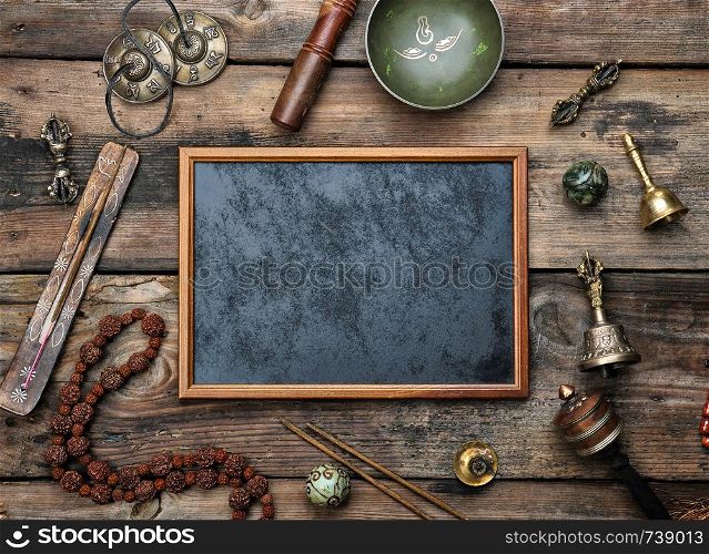 Empty wooden frame and copper singing bowl, prayer beads, prayer drum and other Tibetan religious objects for meditation and alternative medicine on a brown wooden background, copy space