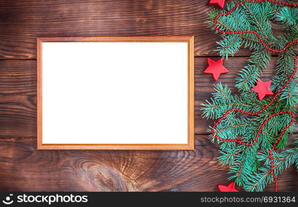 empty wooden frame on a brown wall, next to a green spruce branch and Christmas decor