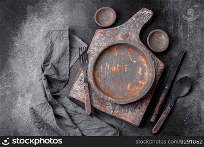 Empty wooden plate, knife, fork and cutting board set on textured concrete background