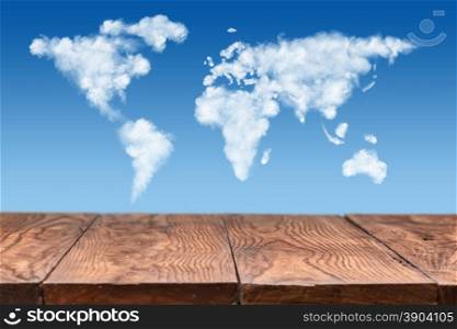empty wooden table with world map made of white puffy clouds on sky as background. wooden table with world map made of clouds on sky
