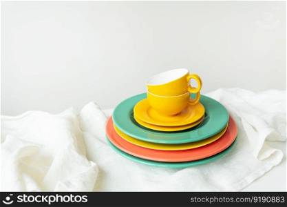 Empty yellow cups and brightly colored plates on a white table covered with a linen tablecloth. Empty yellow cups and brightly colored plates on a white table covered with a linen tablecloth.