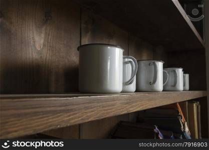 Enamel mugs on solid wooden shelf, natural light.