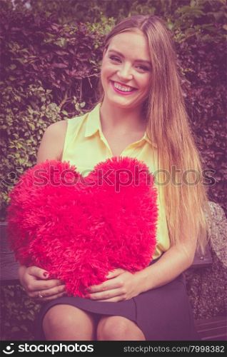 Enamored woman with big red heart. Love and feelings. Happy enamoured woman sitting on bench with big red heart in hands. Beautiful smiling girl in park.
