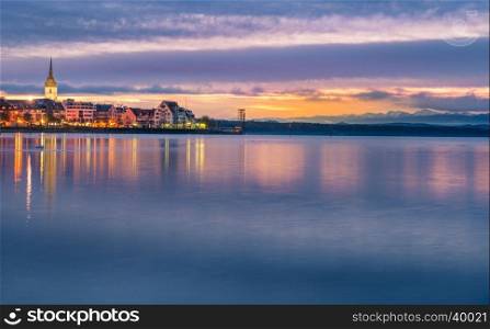 Enchanting landscape with a colorful sky reflected in the water of the Bodensee lake, as the sun is coming up, over Friedrichshafen town, Germany.