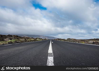 Endless road to Timanfaya National park in Lanzarote, Canary Ispands, Spain, Europe, Africa. Volcanic, black sand, harsh, tough, inhospitable, dry, sub-tropical, desert landscape.