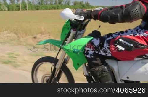 Enduro racer in motorcycle protective gear riding dirt bike, vehicle shot side view