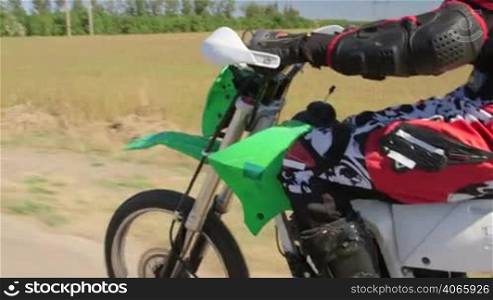 Enduro racer in motorcycle protective gear riding dirt bike, vehicle shot side view