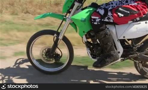 Enduro racer riding dirt bike on track, vehicle shot side view tilt up