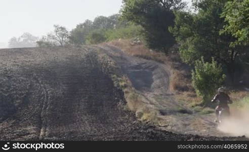 Enduro racer riding motorcycle on dirt track kicking up dust long shot