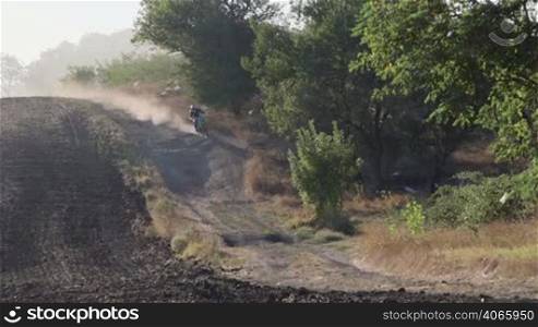 Enduro racer riding motorcycle on dirt track kicking up dust long tracking shot