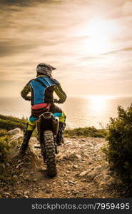 Enduro racer sitting on his motorcycle watching the sunset.