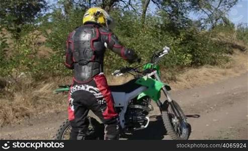Enduro racer starting engine of his motorbike riding away on dirt track tracking shot