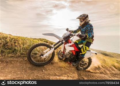 Enduro rider climbing a steep slope against a beautiful sunset on a seascape
