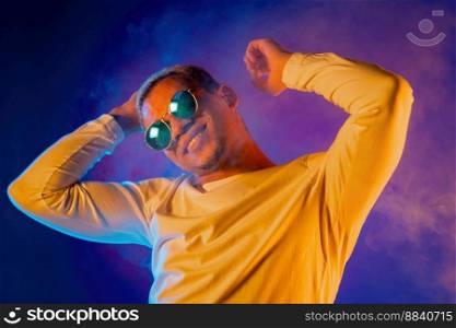 Energetic african american man dancing on colorful background under neon light. Portrait of stylish guy with dyed white curly hairstyle and round mirror eyewear. High quality photo. Energetic african american man dancing on colorful background under neon light. Portrait of stylish guy with dyed white curly hairstyle and round mirror eyewear