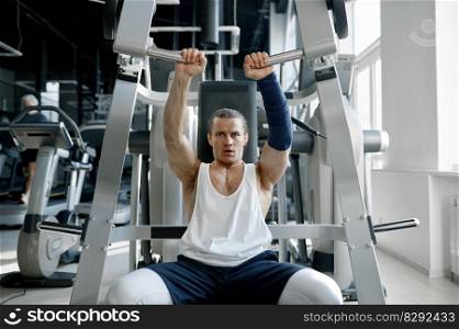 Energetic masculine sportsman working arms pumping muscles on training apparatus at sport gym. Energetic masculine sportsman working arms on training apparatus at sport gym