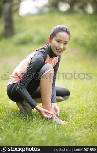 Energetic young woman tying her shoes on the lawn