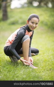 Energetic young woman tying her shoes on the lawn