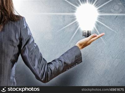 Energy concept. Rear view of businesswoman holding light bulb in palm