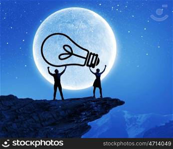 Energy concept. Silhouettes of young couple at night holding bulb
