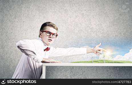 Energy concept. Young man in glasses and miniature of windmills on table