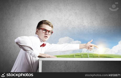 Energy concept. Young man in glasses and miniature of windmills on table