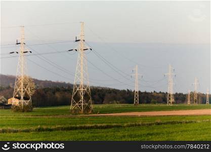 Energy. High voltage post. Electricity pylons power lines high-voltage towers on green field.