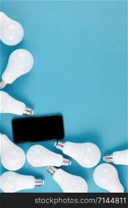 Energy-saving and eco-friendly life in conceptual frame pattern. Creative top view flat lay of LED light bulbs and modern smartphone mockup composition with copy space on blue background minimal style