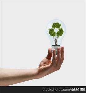 Energy saving. Image of human hand holding bulb with recycle symbol inside