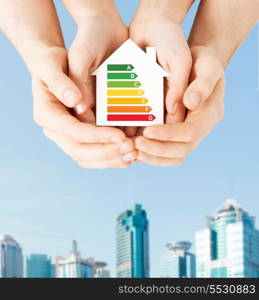 energy saving, real estate and family home concept - closeup of couple hands holding white paper house with energy efficiency rating