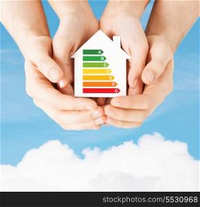 energy saving, real estate and family home concept - closeup of couple hands holding white paper house with energy efficiency rating