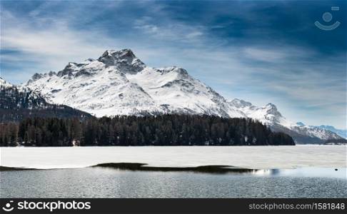 Engadin St. Moritz Mountain landscape near the thaw with lake half frozen and half water.